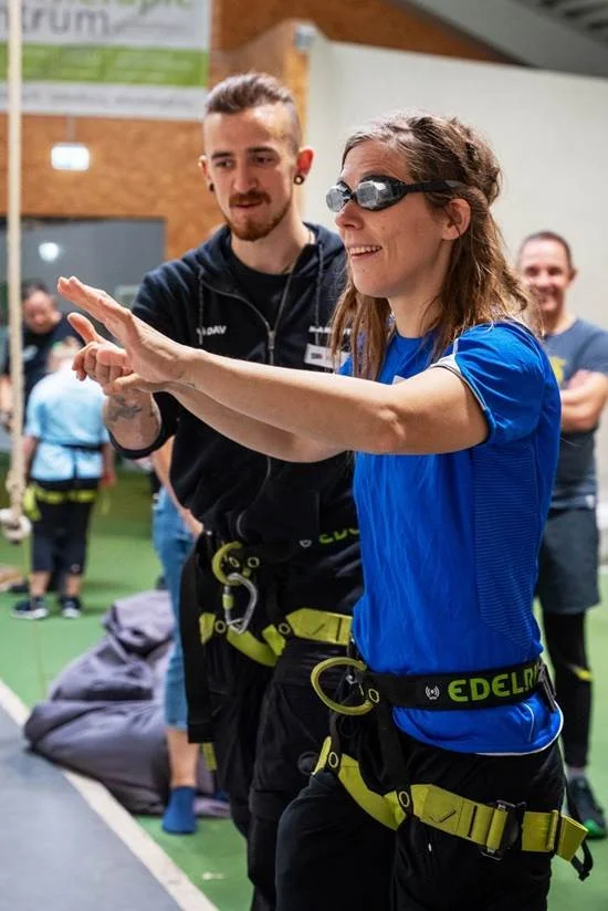 Eine Kletterin bei einer Simulation einer Sehbehinderung, daneben steht ein Trainer | © Kletterzentrum