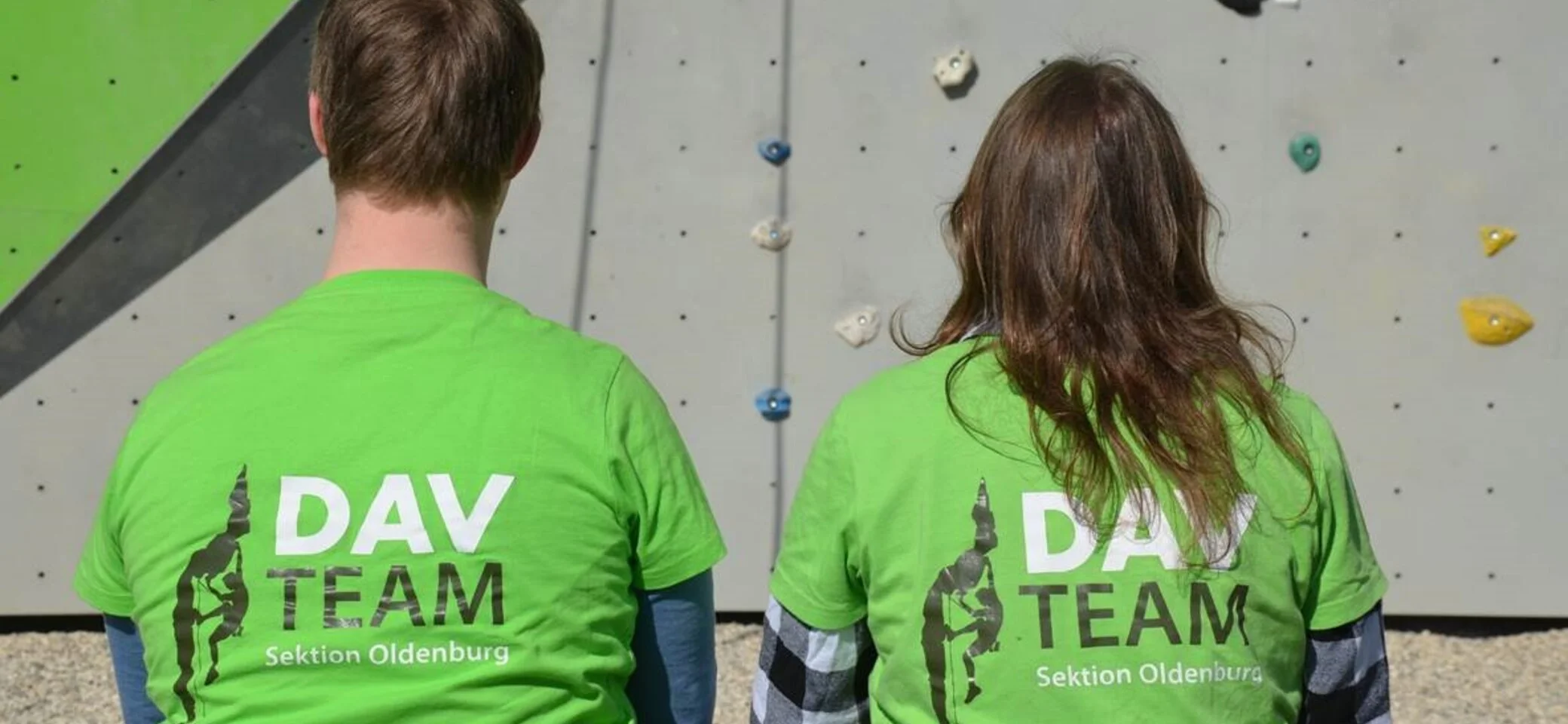 Zwei Kletterer sitzen mit dem Rücken zur Kamera, auf den Shirts steht DAV Team  | © Ralf Holtgrefe