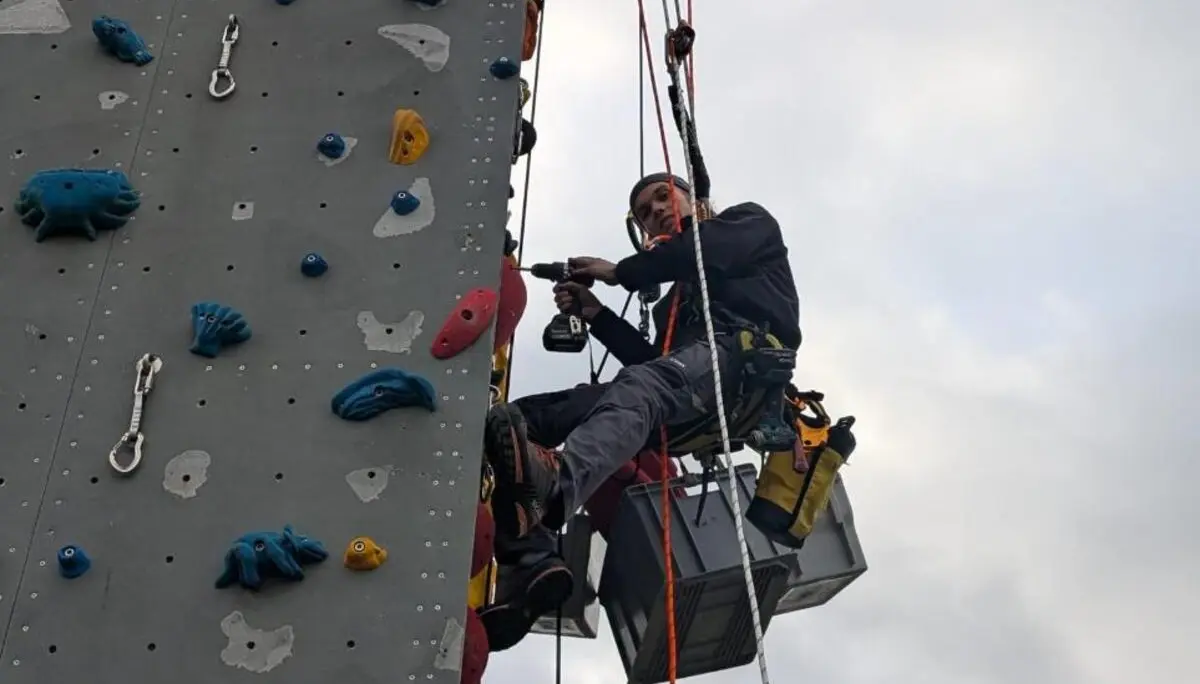 Ein Kletterer hängt am Seil am Turm und schraubt Routen | © Kletterzentrum