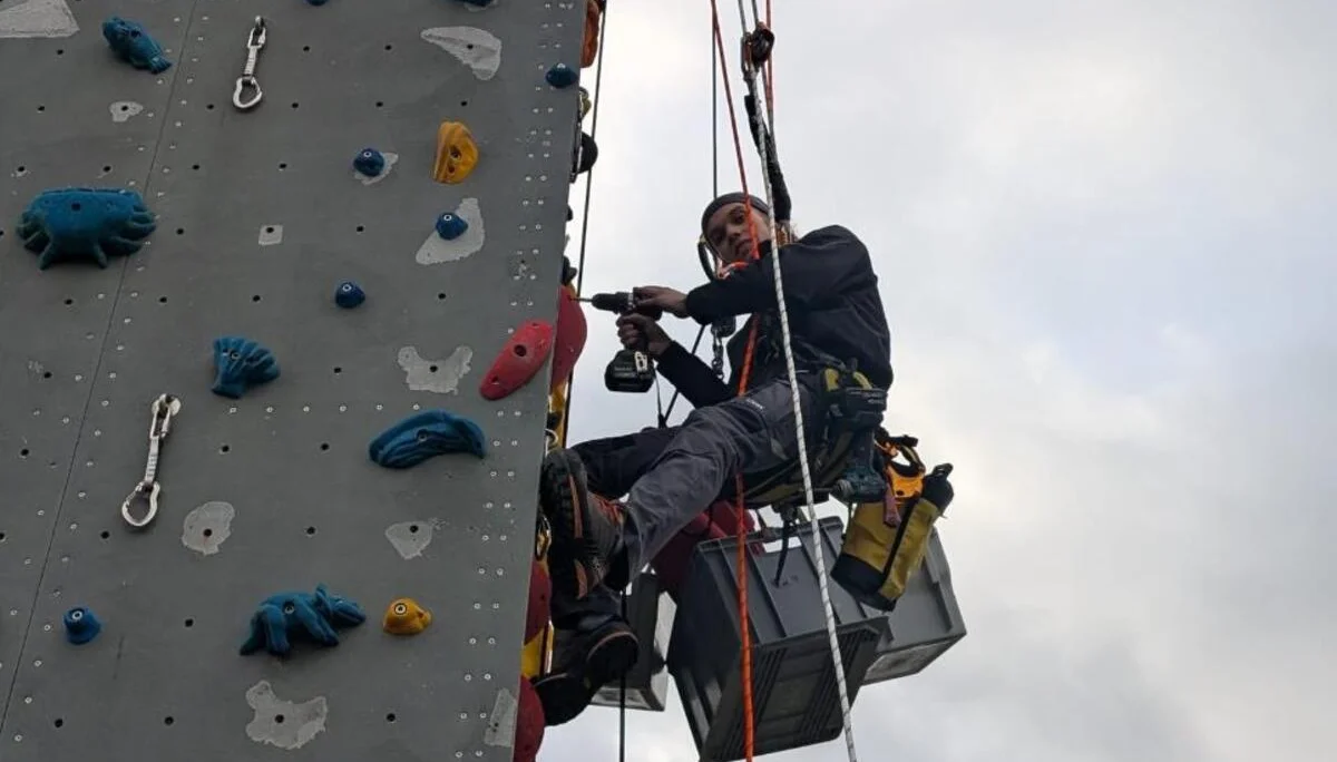 Ein Kletterer hängt am Seil am Turm und schraubt Routen | © Kletterzentrum