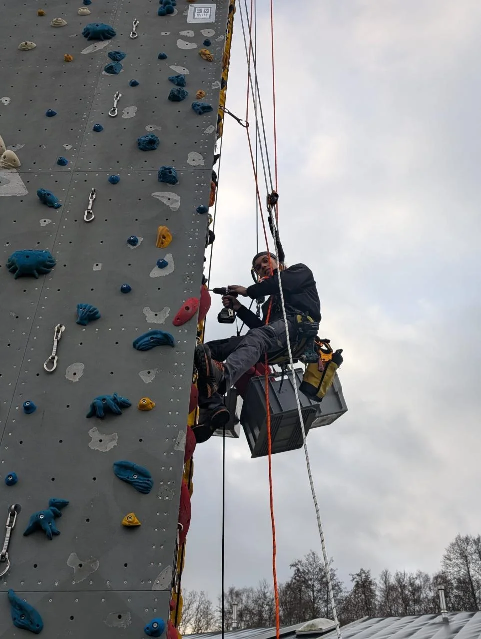 Ein Kletterer hängt am Seil am Turm und schraubt Routen | © Kletterzentrum