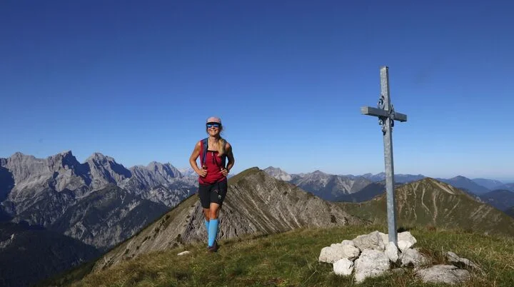 Eine Bergwanderin im Karwendel Gebirge neben einem Gipfelkreuz | © Michael Pröttel